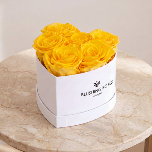 White box with yellow roses on a marble surface, featuring ' Blushing Roses' brand.