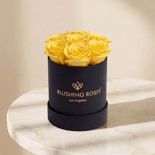 Black box with yellow roses labeled BLUSHING Roses Los Angeles' on a marble surface.