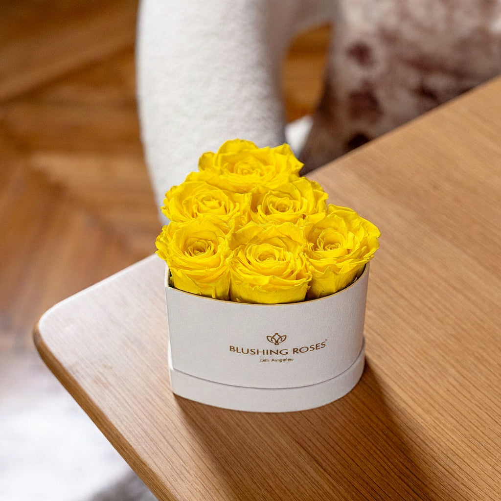 Yellow roses in a white box on a wooden surface with 'BLUSHING Roses' branding.