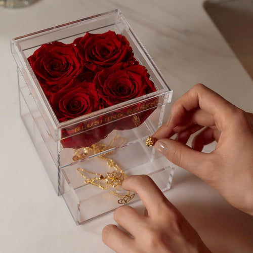 Real preserved red roses in clear acrylic drawer box, elegant forever flower arrangement for luxury gifting and modern décor | Blushing Roses , Clear box with preserved red roses and a gold necklace, held by hands on a light surface.