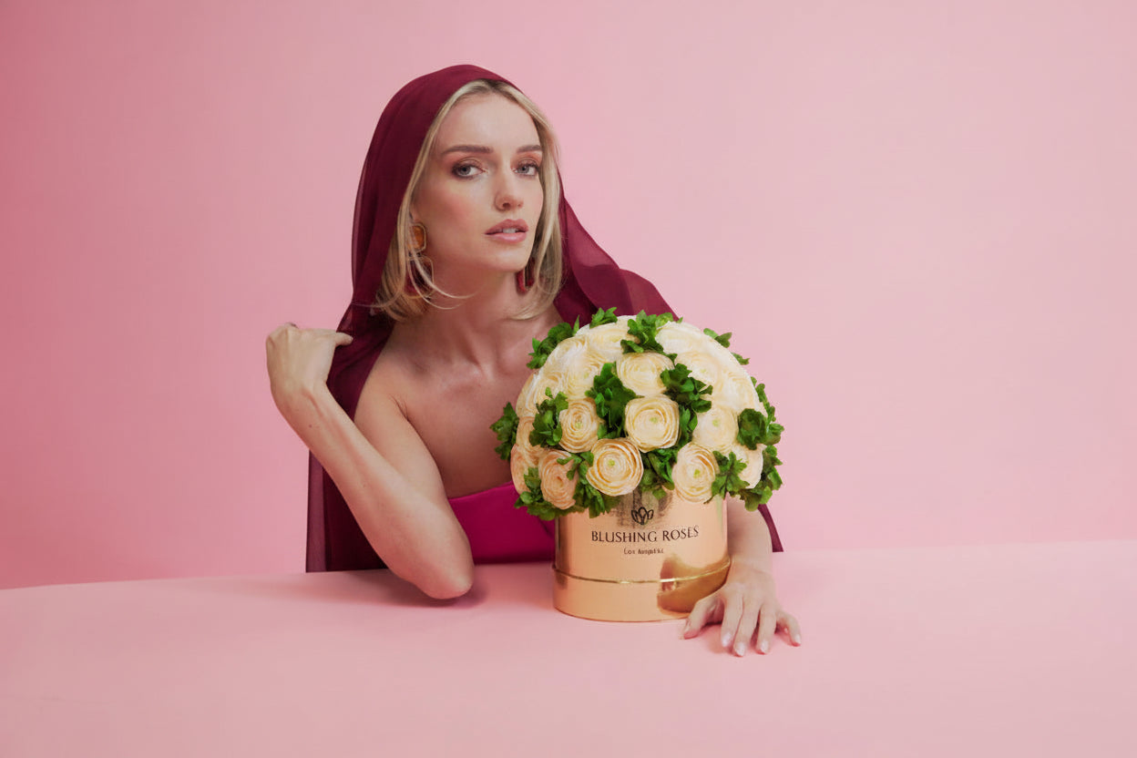 Modern black flower box with peach eternal roses and green hydrangeas, elegant preserved floral gift arrangement | Blushing Roses ; great for Mother’s Day; Woman holding a bouquet of flowers inside a decorative gold box on a pink background